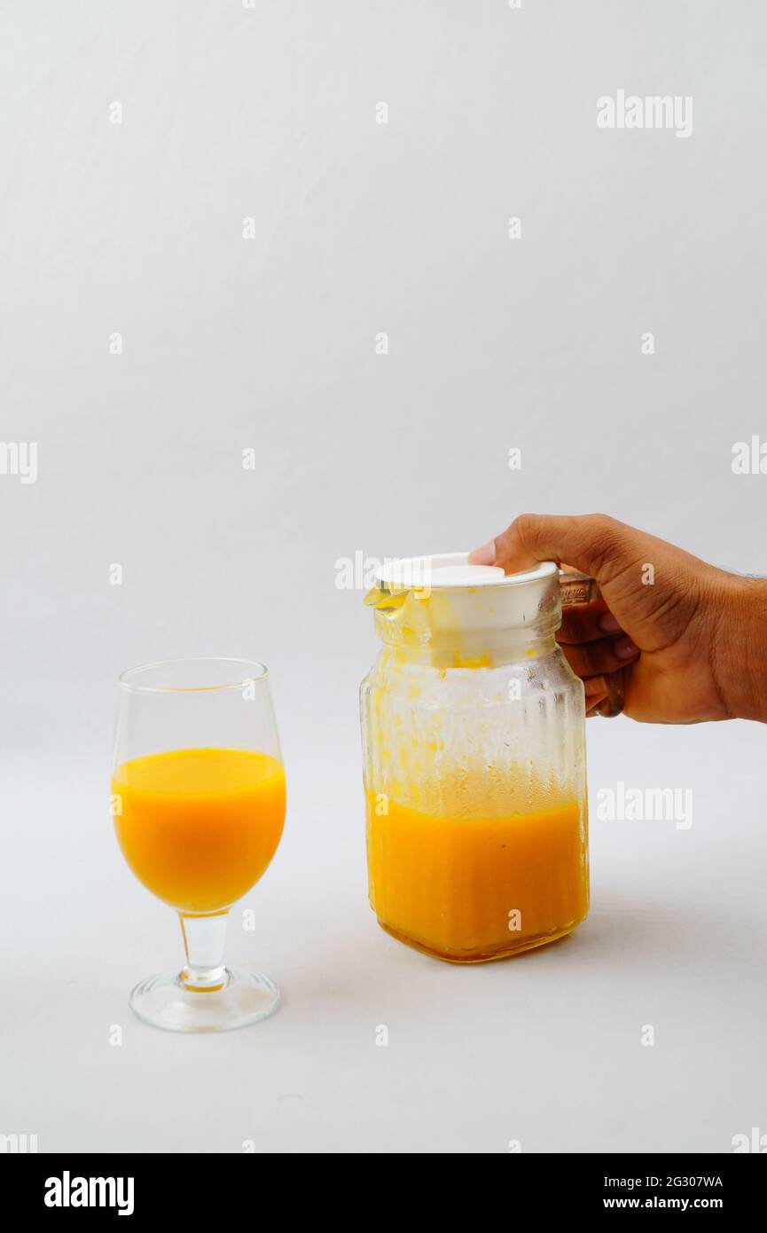 Un primo piano di una persona che tiene una caraffa di succo di mango fresco e bicchiere Foto Stock