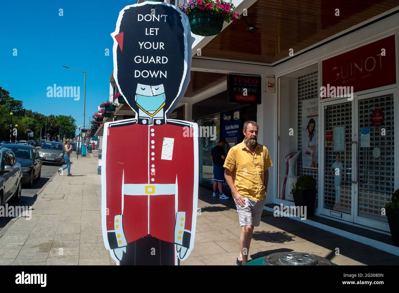 Ascot, Berkshire, Regno Unito. 13 giugno 2021. La gente cammina oltre non lasciare la vostra guardia giù le indicazioni in Ascot High Street. Il numero di risultati positivi di Covid-19 nel Berkshire è in aumento su base giornaliera mentre la variante indiana di Covid-19 si sposta in tutto il Regno Unito. Di conseguenza, Boris Johnson dovrebbe annunciare domani che la revoca delle restrizioni di blocco di Covid-19 previste per il 21 giugno 2021 sarà messa in attesa per un altro mese. Credit: Maureen McLean/Alamy Live News Foto Stock