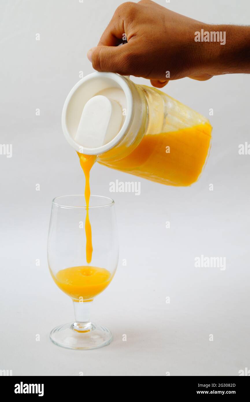 Un primo piano di una persona che versa il succo di mango fresco in un bicchiere Foto Stock