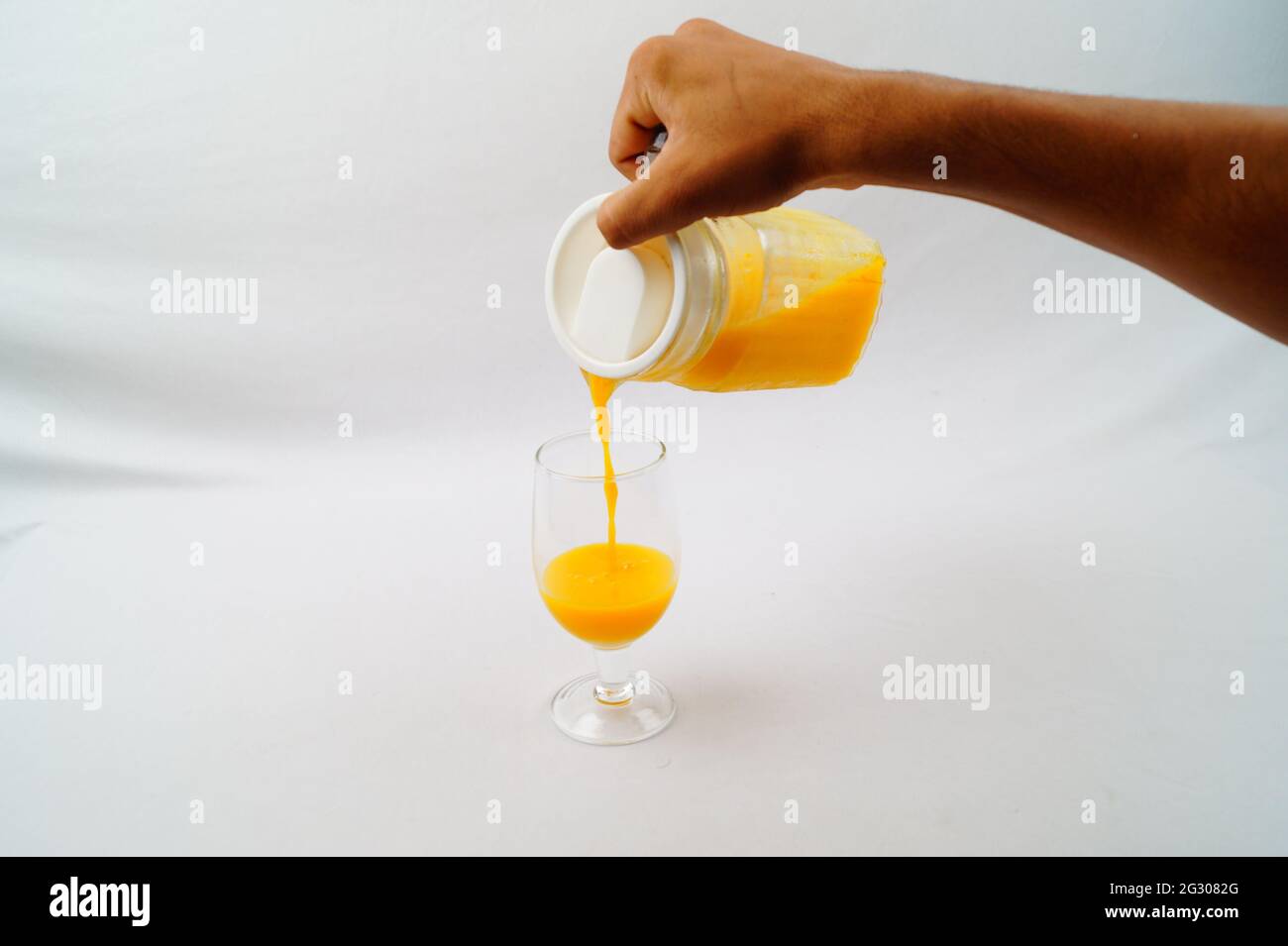 Un primo piano di una persona che versa il succo di mango fresco in un bicchiere Foto Stock