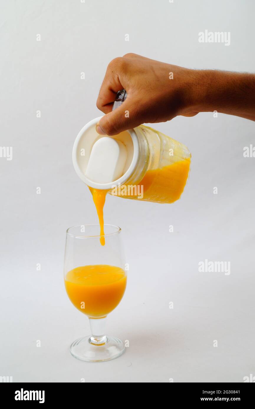Un primo piano di una persona che versa il succo di mango fresco in un bicchiere Foto Stock