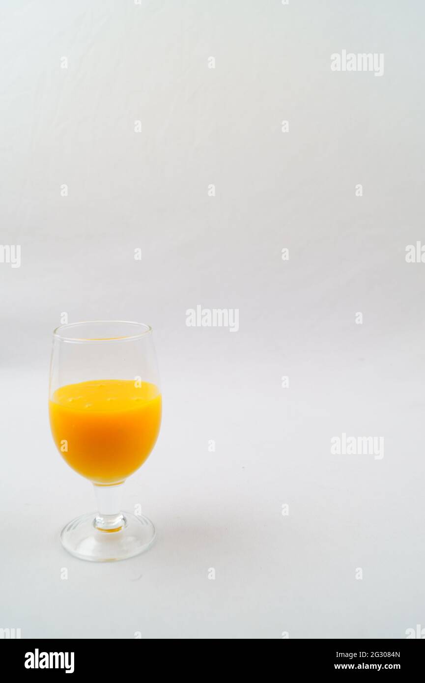 Una selezione di un bicchiere di succo di mango fresco su una superficie bianca Foto Stock