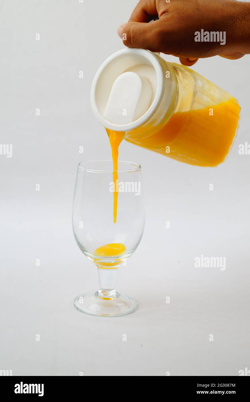 Un colpo closeup di una persona che versa il succo di mango fresco in un bicchiere su una superficie bianca Foto Stock