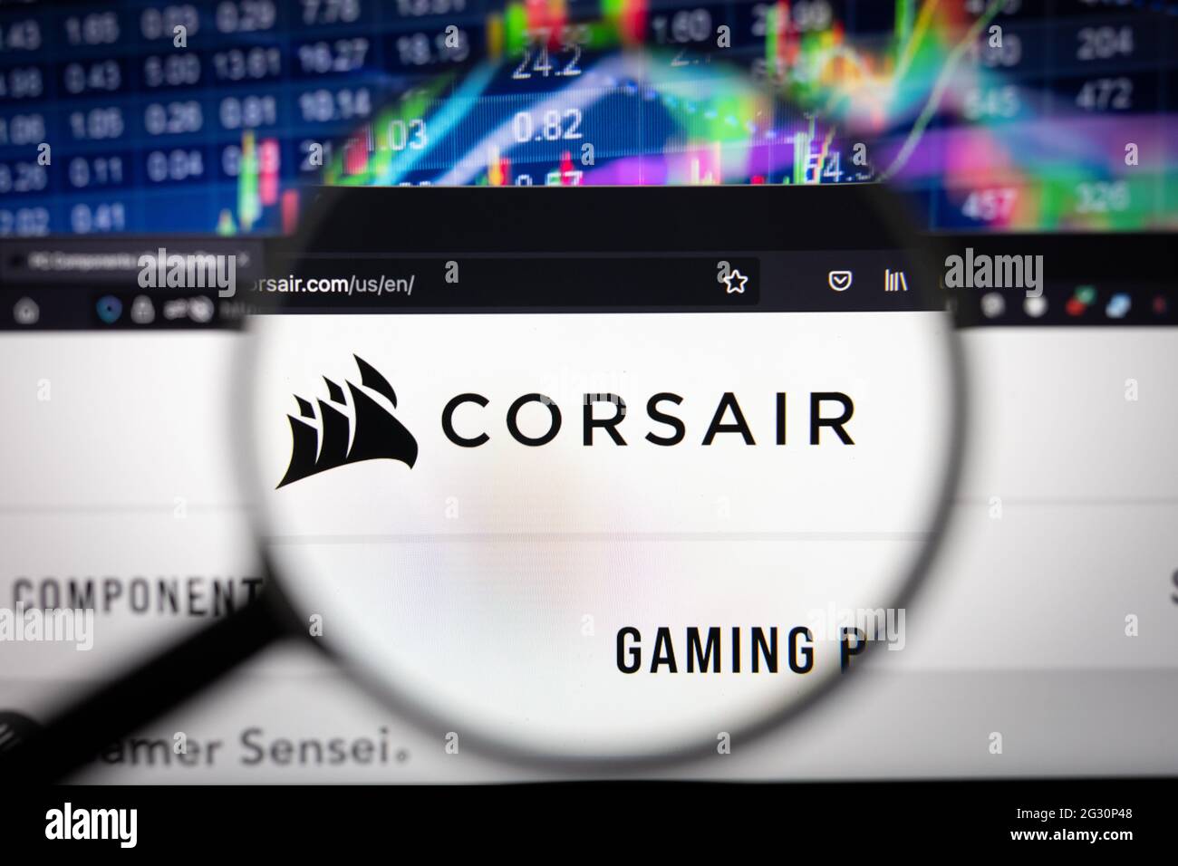 Logo aziendale Corsair su un sito web con sviluppi sfocati del mercato azionario in background, visto su uno schermo del computer attraverso una lente di ingrandimento Foto Stock