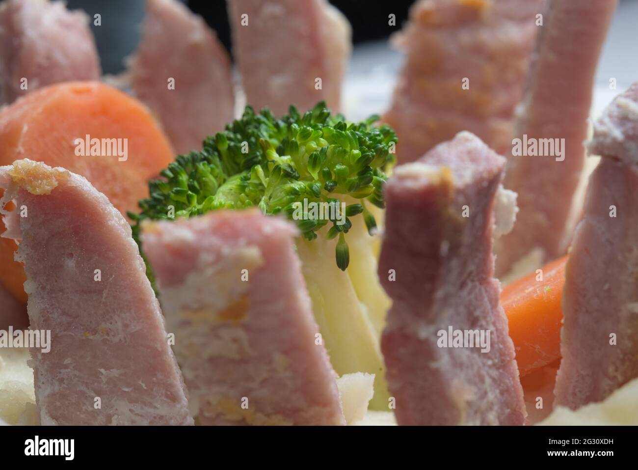 Vista laterale del pasto serale presentato in modo strano. Le strisce e le fette di gammon erano in posizione verticale nella purea di patate bianca, concentrandosi sui broccoli con le carote anche. Foto Stock