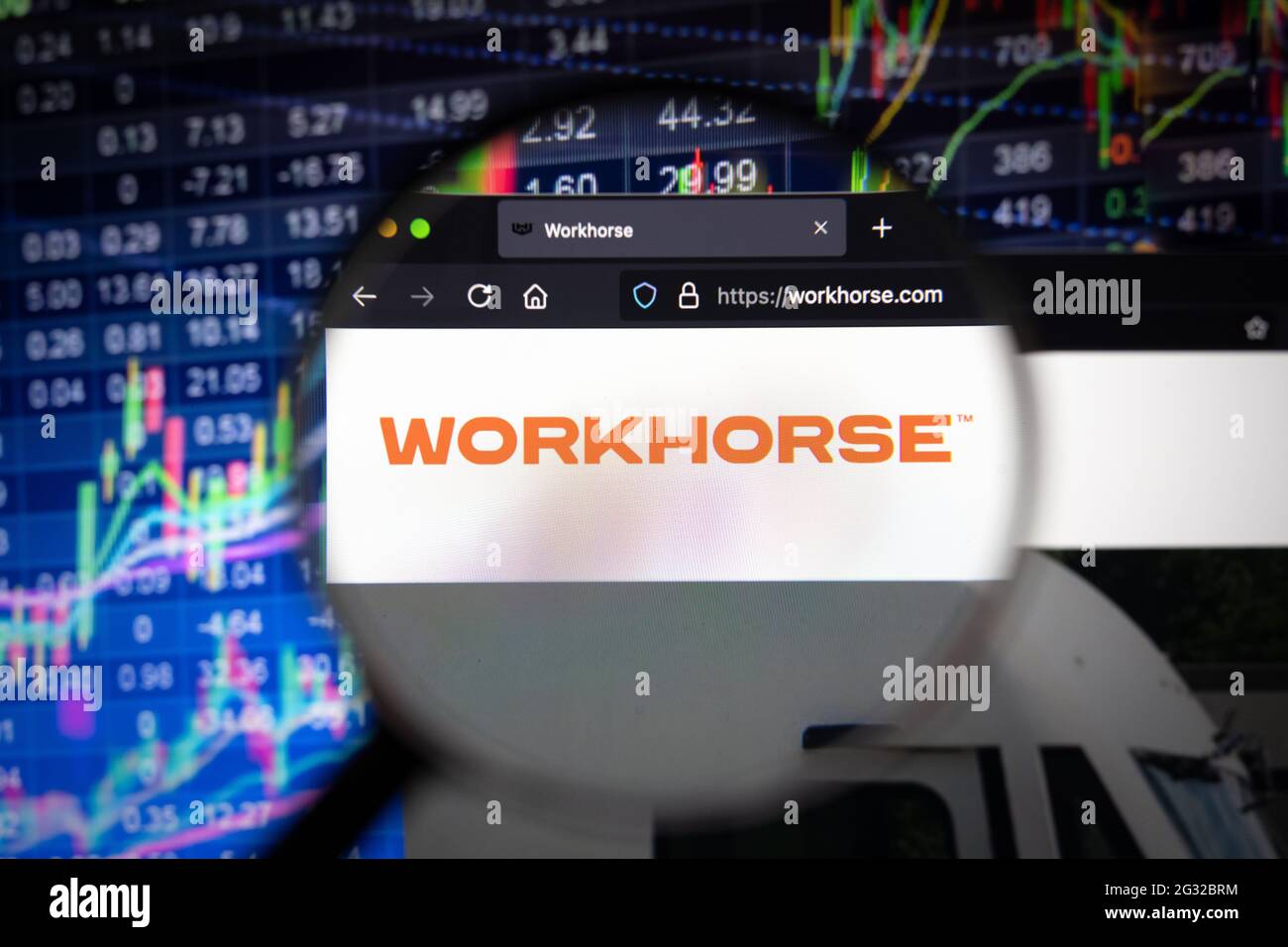 Logo aziendale Workhorse su un sito Web con sviluppi sfocati del mercato azionario in background, visto su uno schermo del computer attraverso una lente di ingrandimento Foto Stock