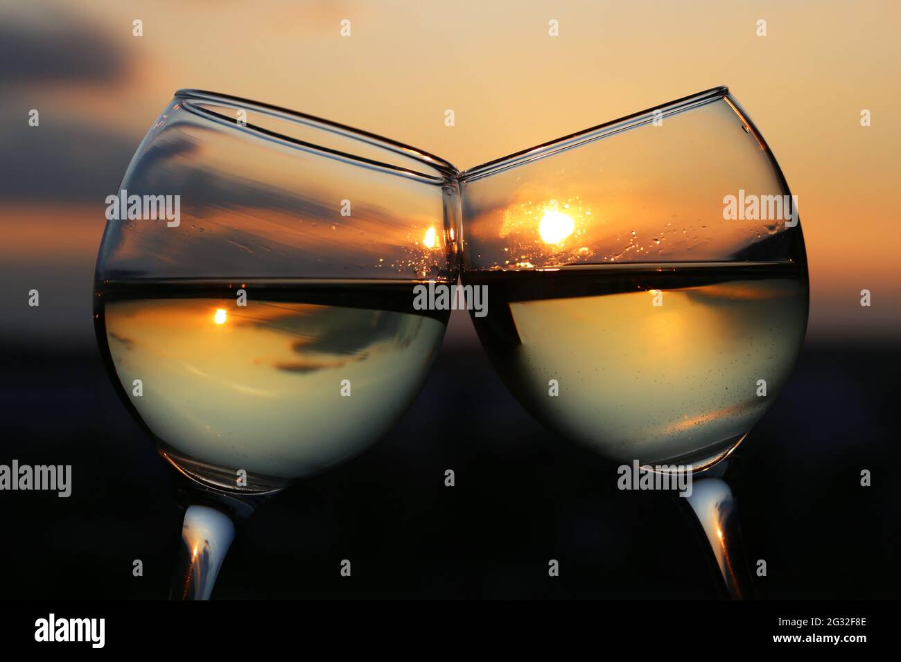 Due bicchieri con vino bianco sullo sfondo del tramonto, il sole e il cielo della sera si riflettono in un bicchiere appannato. Concetto di celebrazione, cocktail romantico, amore Foto Stock
