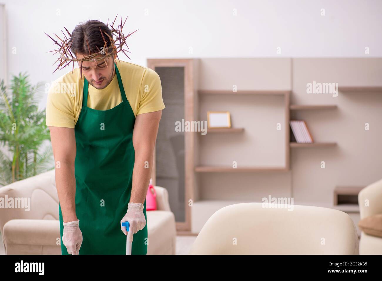 Giovane imprenditore maschio che indossa una corona di prickly sulla testa che fa il lavoro domestico Foto Stock