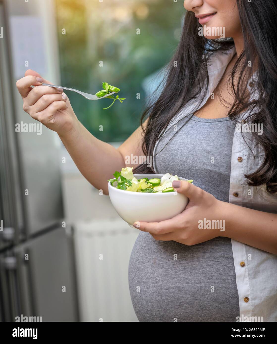 Buona donna incinta con piacere mangiare insalata verde fresca a casa. Parte faccia. Dieta per una futura Madre. Concetto di gravidanza sana. Foto Stock