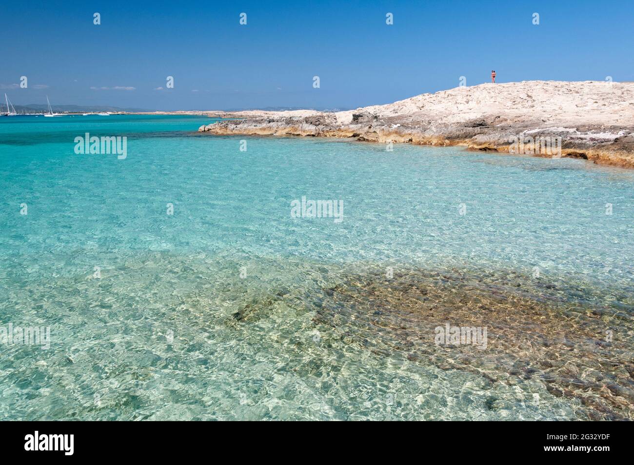 La spiaggia di Ses Illetas, Formentera, Spagna. Una persona nella parte superiore della roccia osserva il mare Mediterraneo dalle acque cristalline Foto Stock