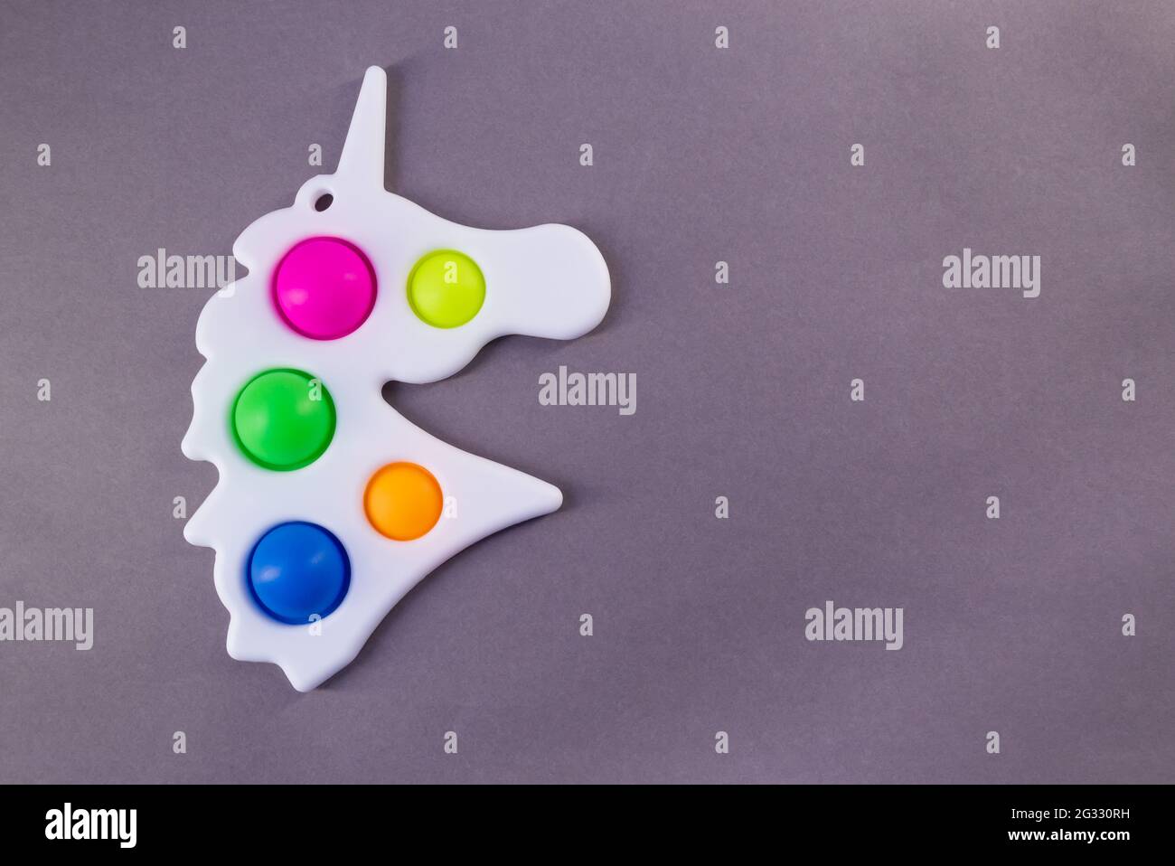 Giocattolo luminoso e colorato semplice Dimple a forma di unicorno. Popolare giocattolo anti stress su sfondo grigio, spazio copia Foto Stock