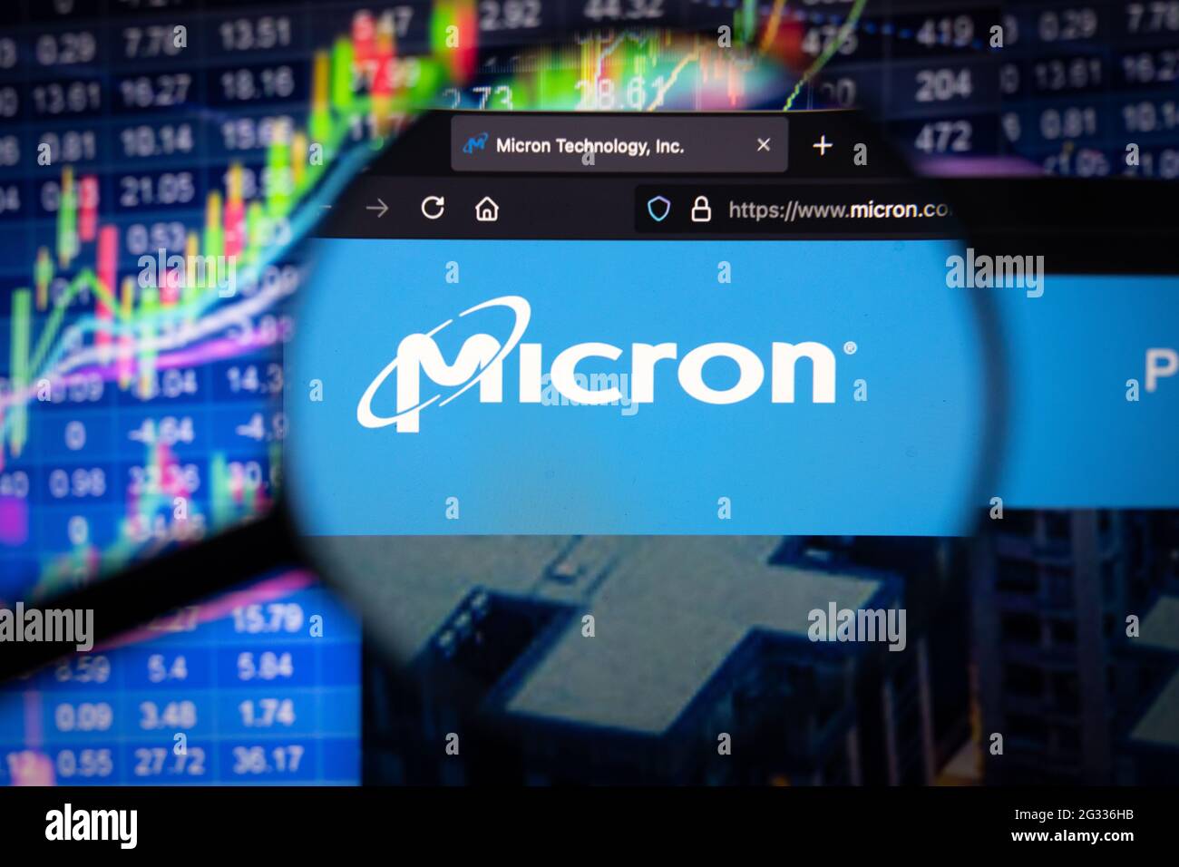 Logo aziendale micron su un sito web con sviluppi sfocati del mercato azionario sullo sfondo, visto su uno schermo del computer attraverso una lente di ingrandimento Foto Stock