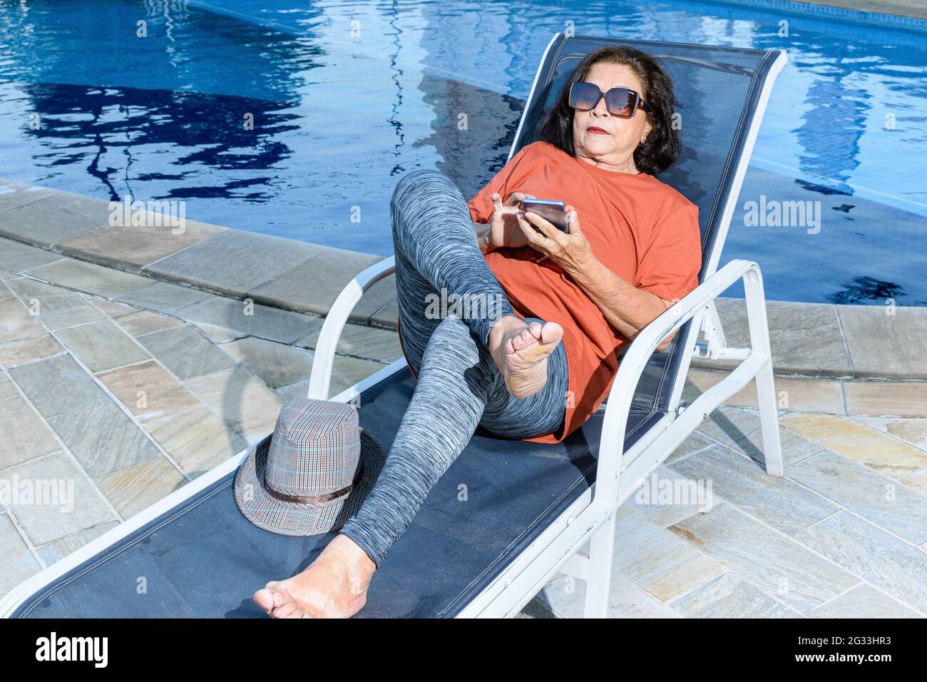 donna di 74 anni seduta su una sedia a sdraio e con il suo smartphone. Foto Stock