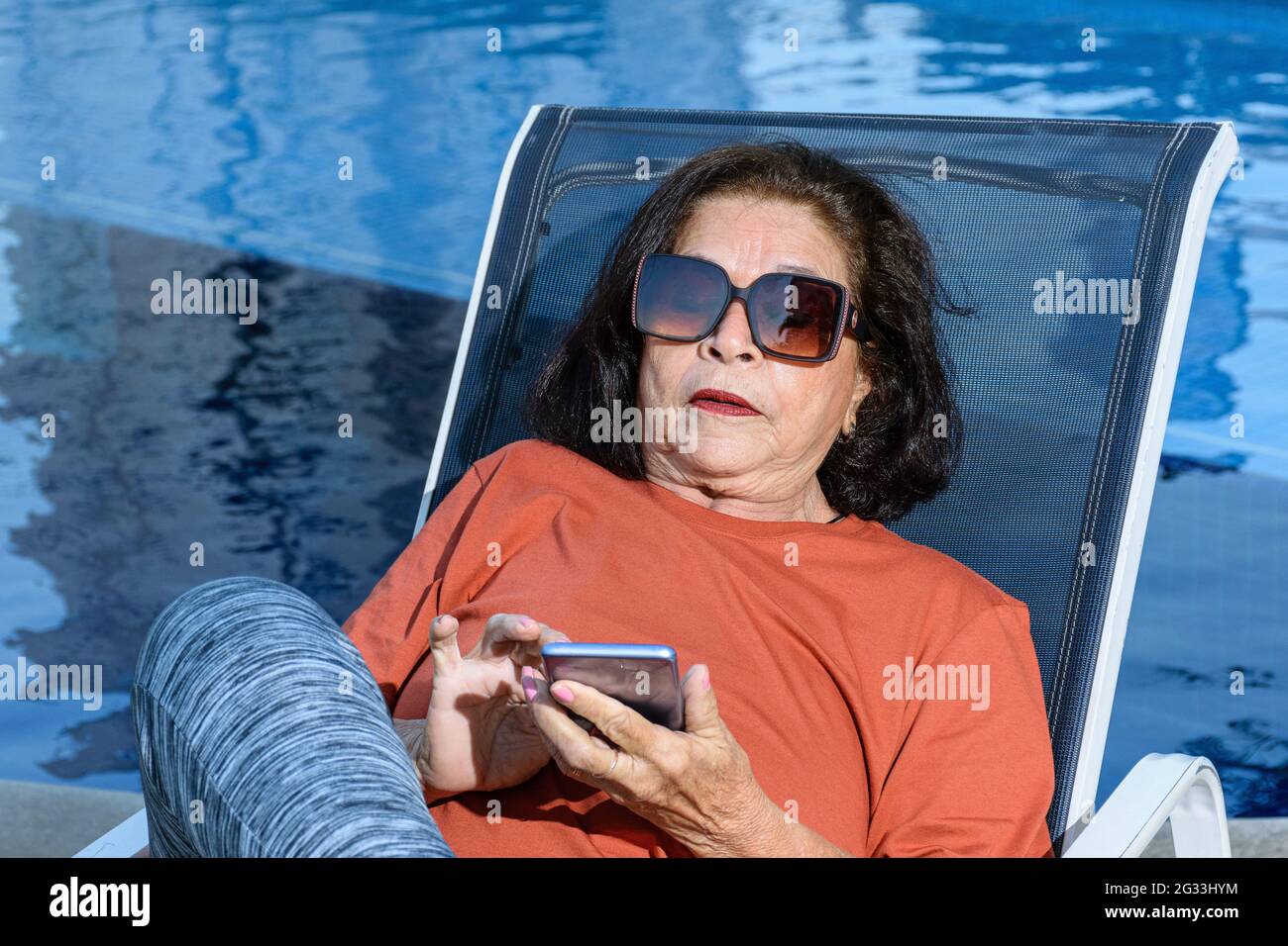 Closeup di 74 anni donna seduta in una sedia a sdraio e utilizzando il suo smartphone. Foto Stock