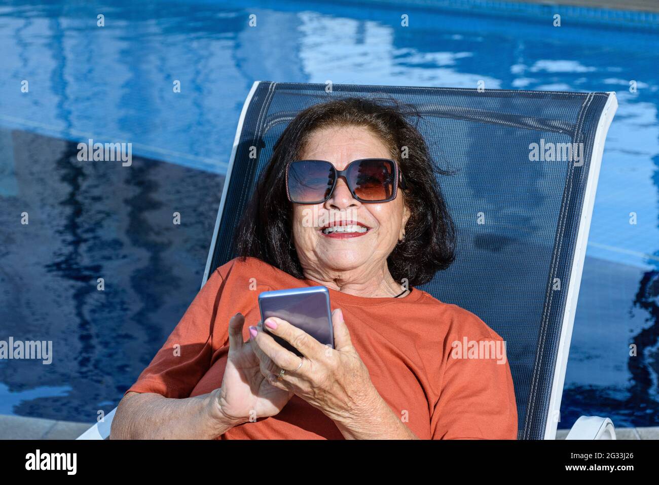 Closeup di 74 anni donna seduta in una sedia a sdraio e utilizzando il suo smartphone. Foto Stock