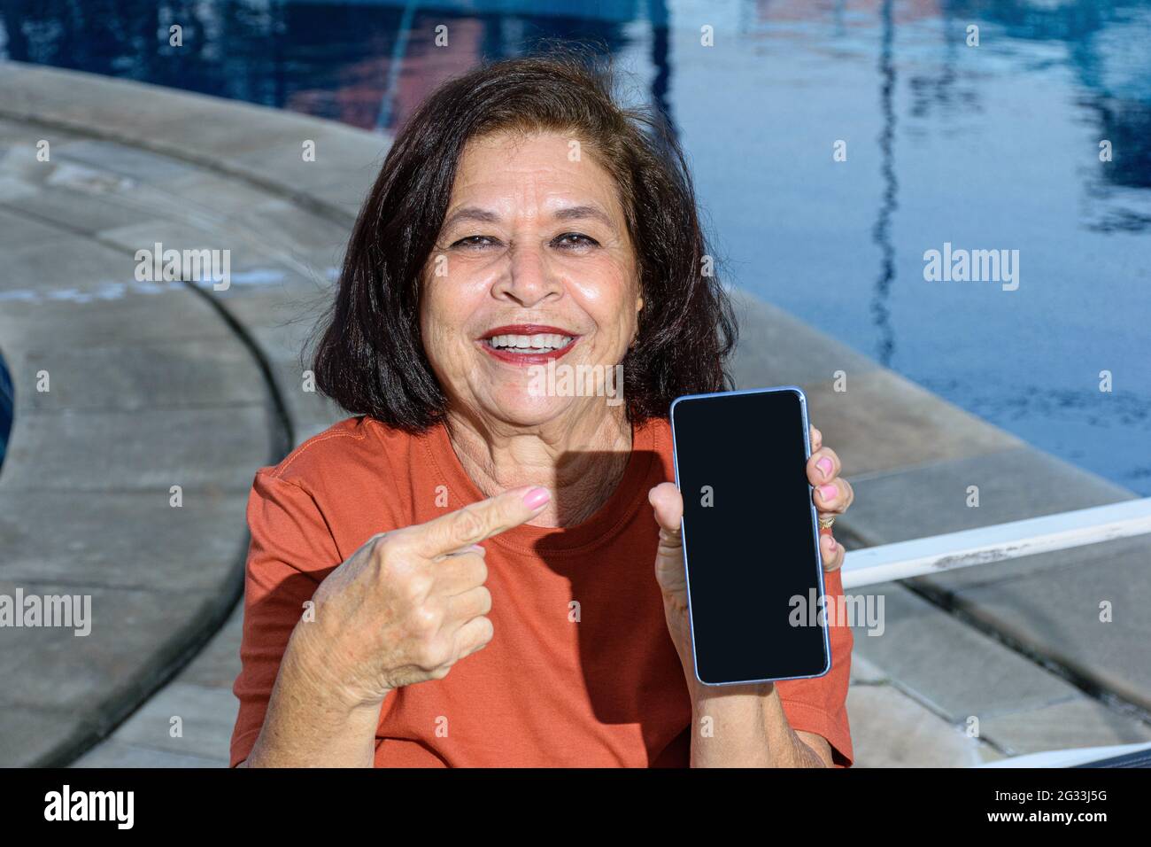 donna di 74 anni che sorride e punta il dito verso il suo smartphone. Foto Stock
