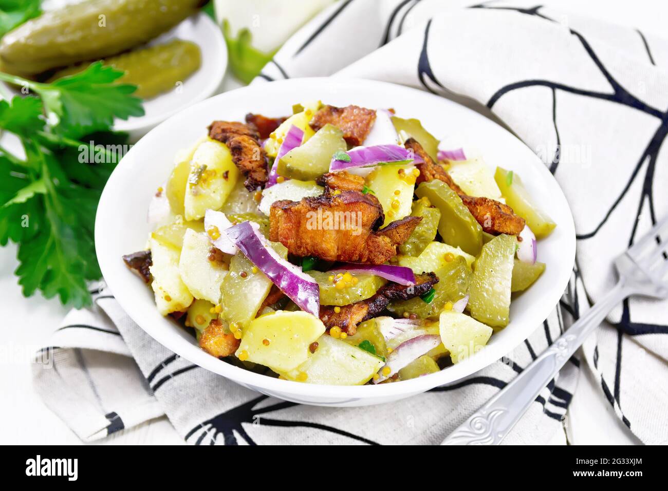 Insalata di patate bollite, pancetta fritta, cipolle rosse e cetrioli sottaceto, condita con senape di grano, spezie e olio vegetale in un piatto su asciugamano aga Foto Stock
