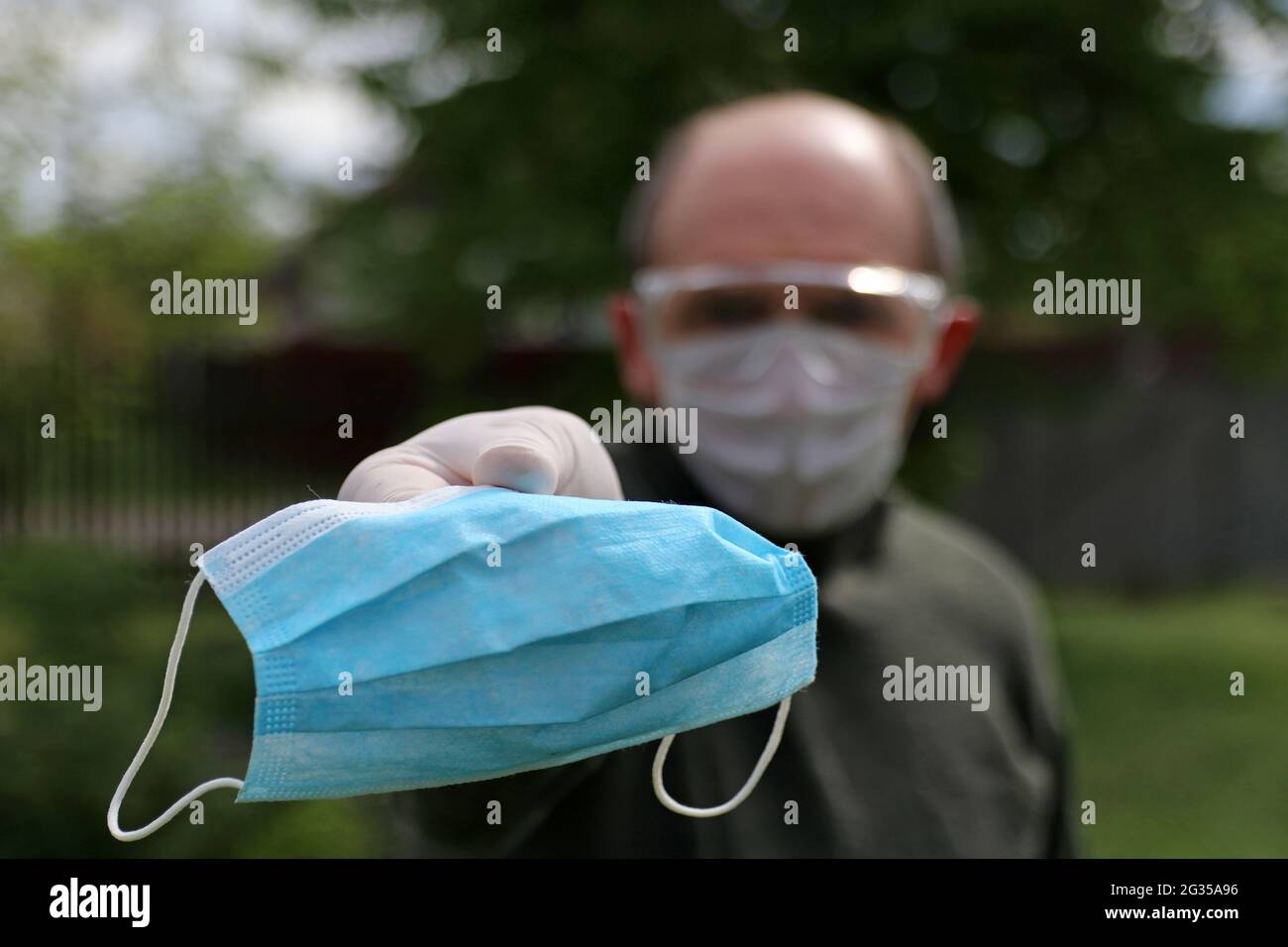 Un uomo non identificabile in una maschera protettiva, occhiali e guanti suggerisce di indossare una maschera medica. Concetto di coronavirus. Foto Stock