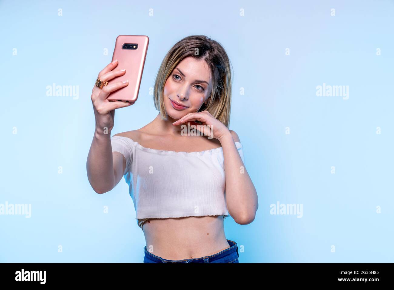 Foto della giovane ragazza caucasica con gli occhi blu chiaro che prende selfie con il suo smartphone - Studio fotografia di bella donna che tiene il suo telefono Foto Stock