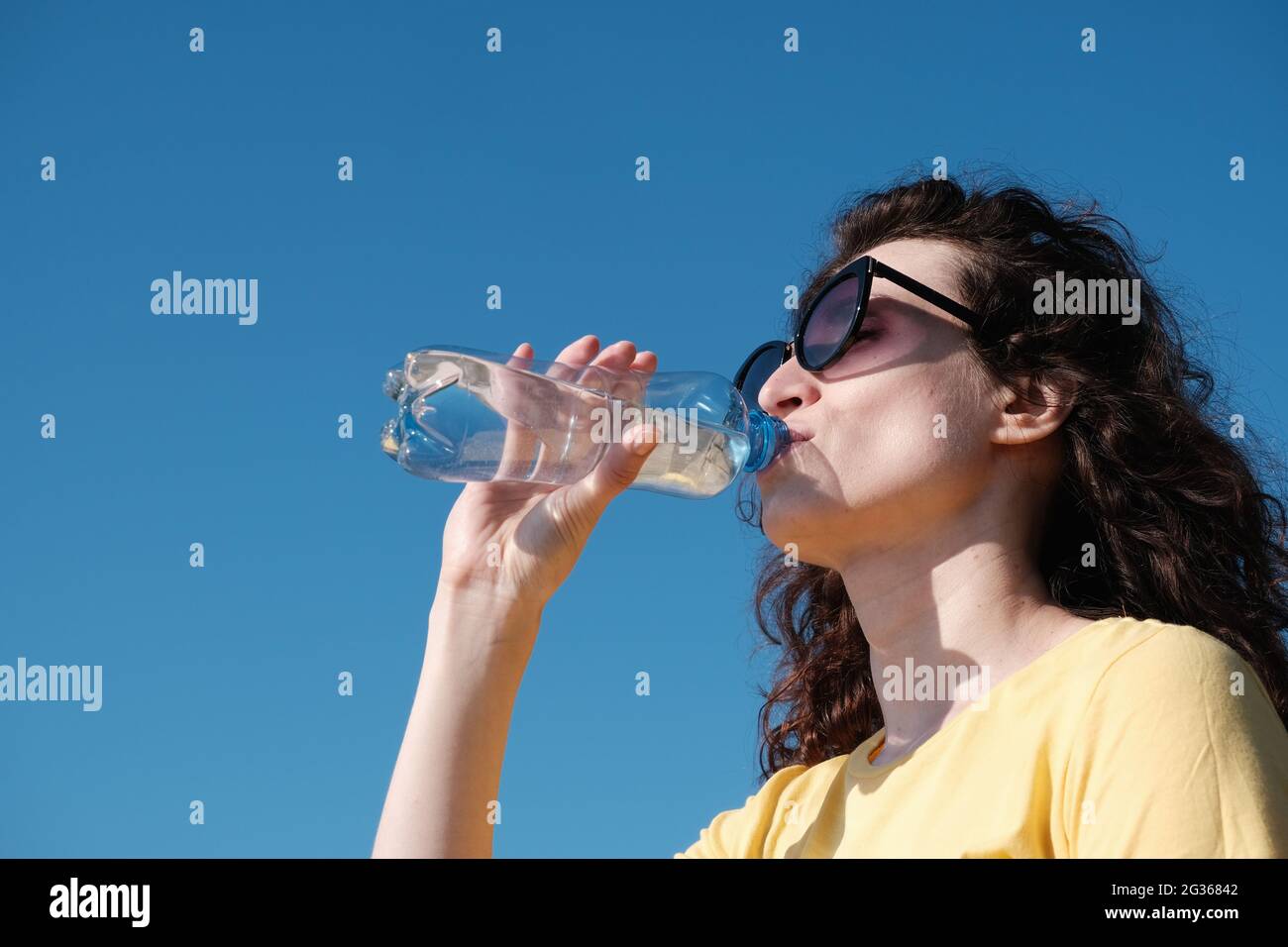 Ragazza con bicchieri beve acqua da una bottiglia in tempo caldo. Foto Stock