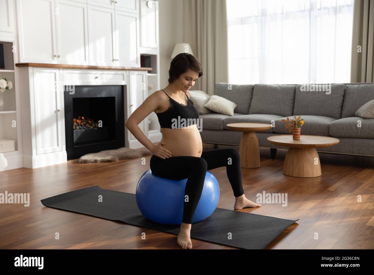 Donna incinta in abbigliamento sportivo seduta su palla da ginnastica, facendo esercizi Foto Stock