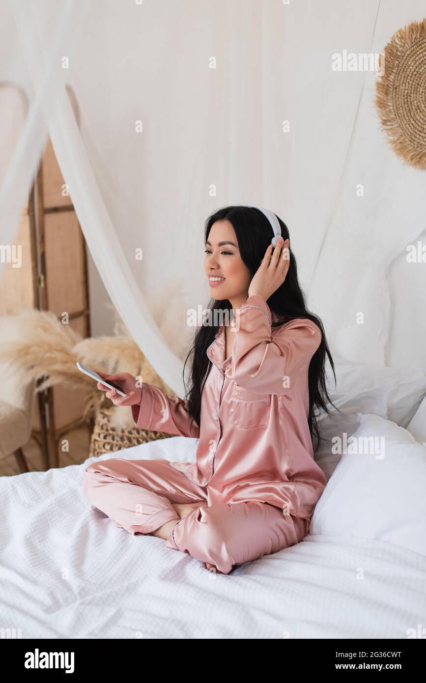 giovane donna asiatica in pigiama di seta rosa seduta a letto con