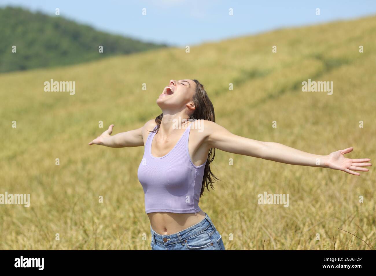 Donna eccitata urlando in un campo di grano che allunga le braccia Foto Stock