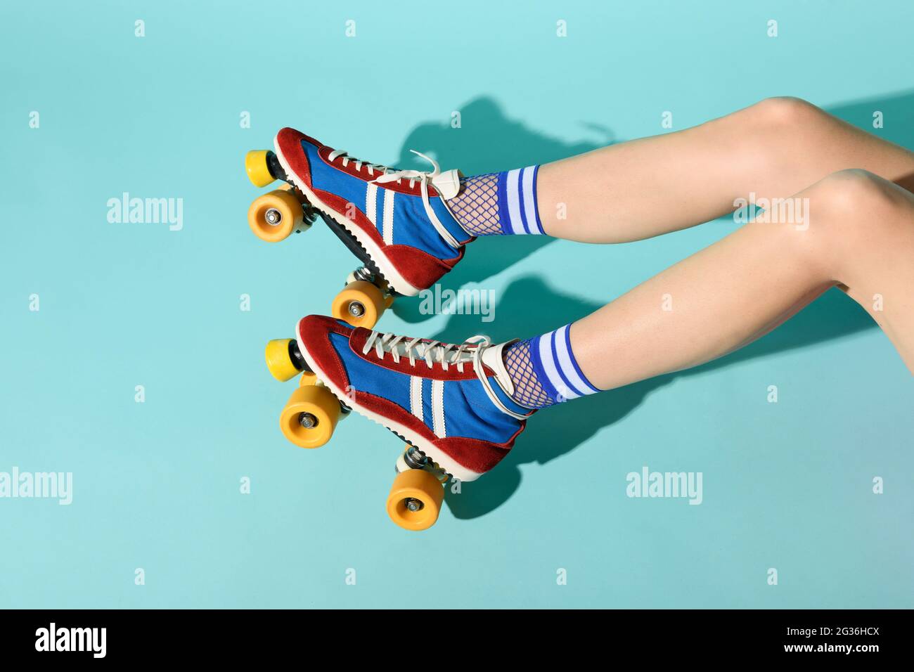 Giovane donna con gambe sottili skinny che indossa colorati pattini a rotelle con ruote gialle e una vista delle sue gambe che si estende da destra su uno sfondo blu Foto Stock
