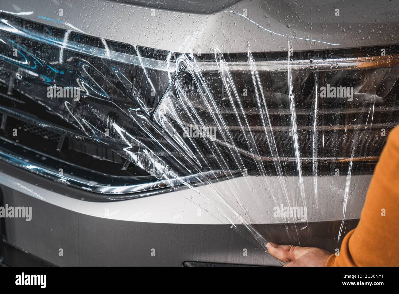 Processo di armatura della cappa con rivestimento in film trasparente in poliuretano anti-ghiaia o PPF in garage di dettaglio auto. Foto Stock