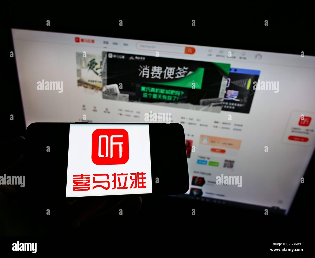 Persona che tiene lo smartphone con il logo della piattaforma radio cinese online Ximalaya sullo schermo di fronte al sito web. Mettere a fuoco il display del telefono. Foto Stock