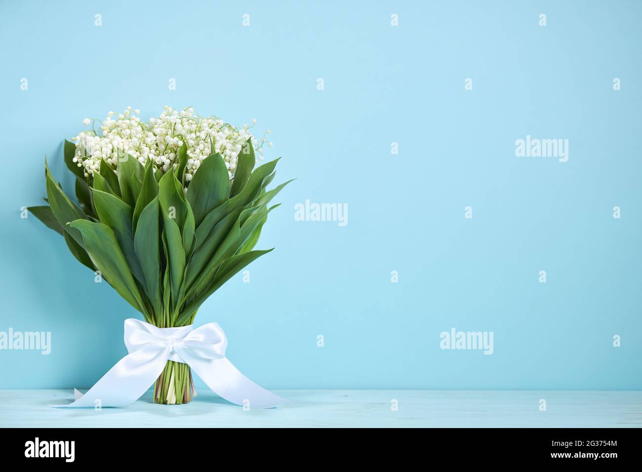 Bouquet di gigli della valle con un nastro bianco su sfondo blu. Concetto di cartolina. Copia spase. Foto Stock