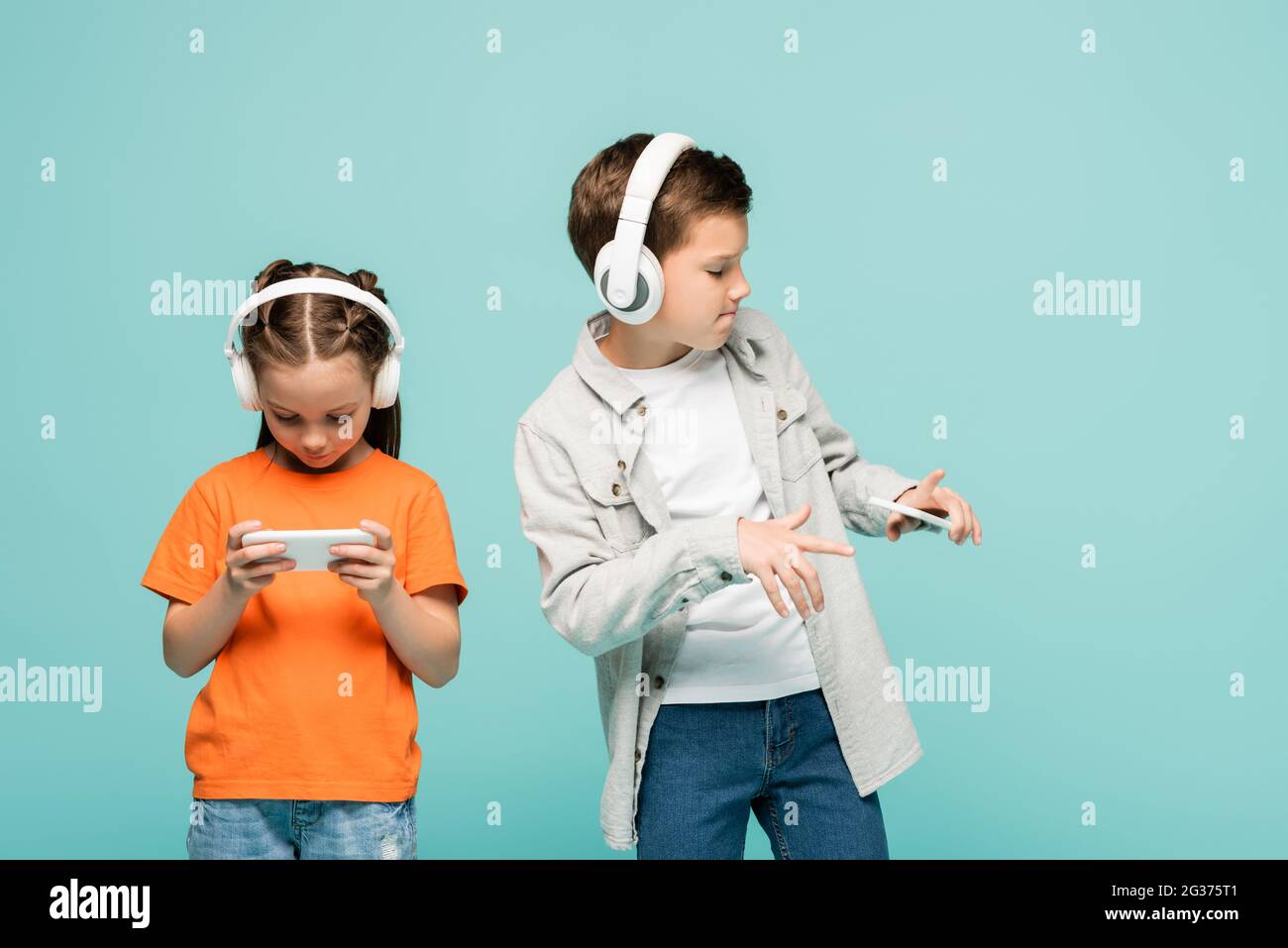 ragazza che usa lo smartphone vicino al ragazzo in cuffie wireless per ascoltare musica mentre balla isolato su blu Foto Stock