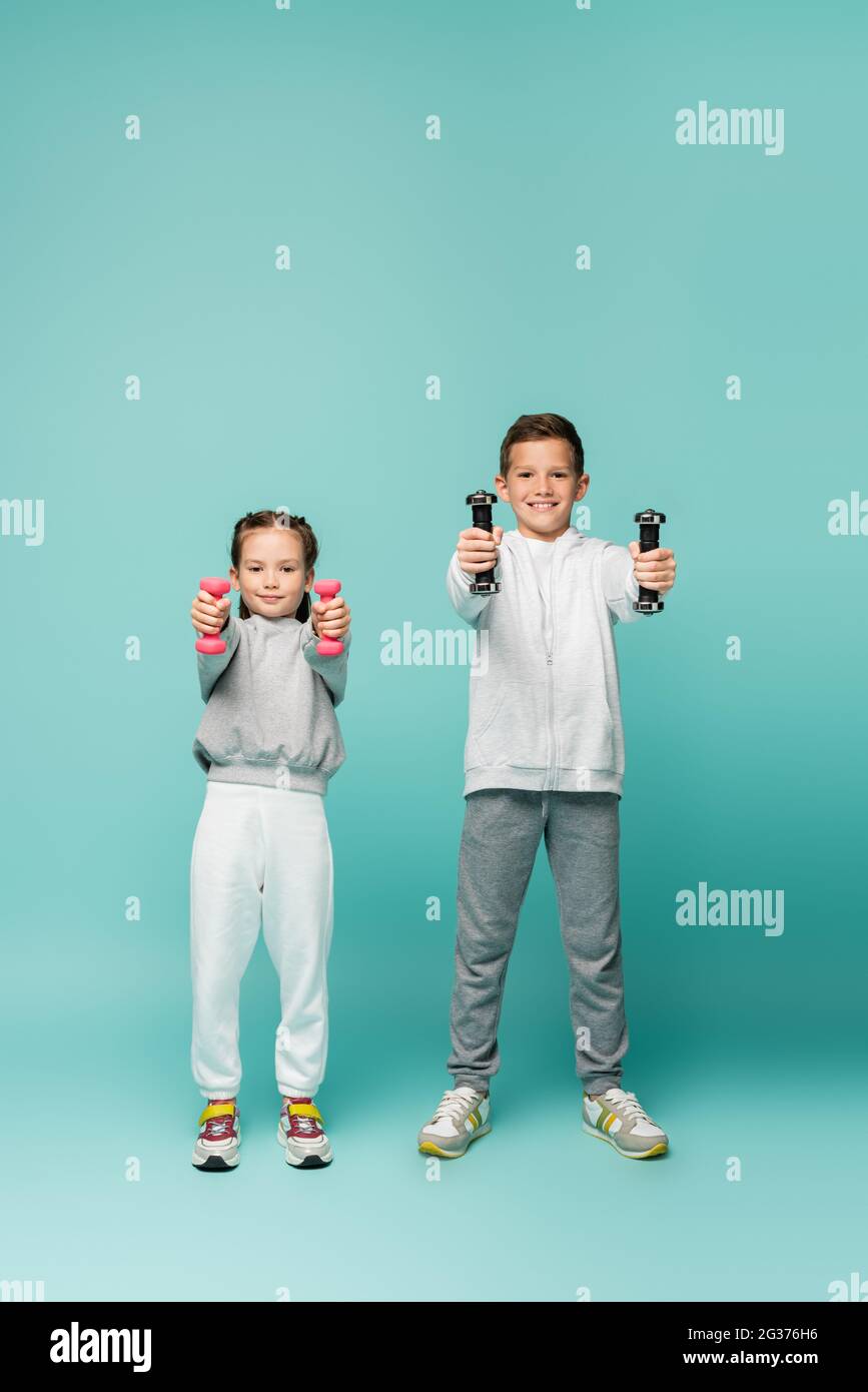 felici i bambini in abbigliamento sportivo e sneakers che si allenano con i manubri blu Foto Stock