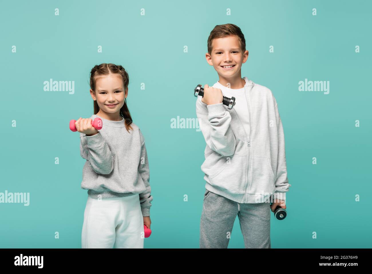felici i bambini in abbigliamento sportivo che si allenano con i manubri isolati su blu Foto Stock
