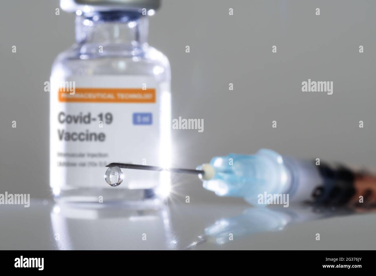 Chiusura della gocciolina sulla punta della siringa con il vaccino COVID-19 e il flaconcino sullo sfondo. Vaccinazioni, Covid-19, industria farmaceutica e salute conce Foto Stock