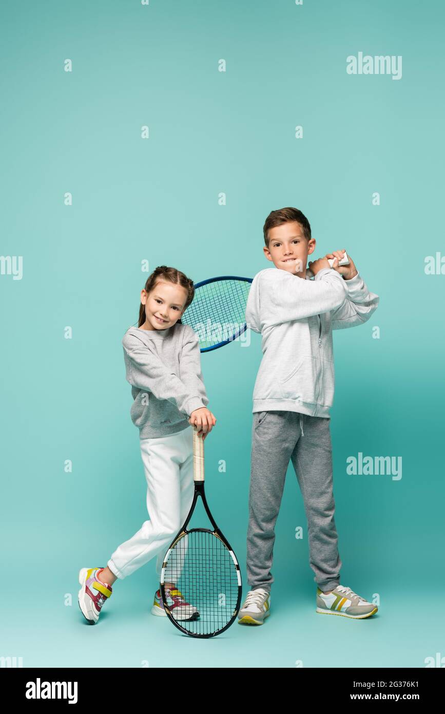 bambini allegri in abbigliamento sportivo in piedi con racchette da tennis su blu Foto Stock