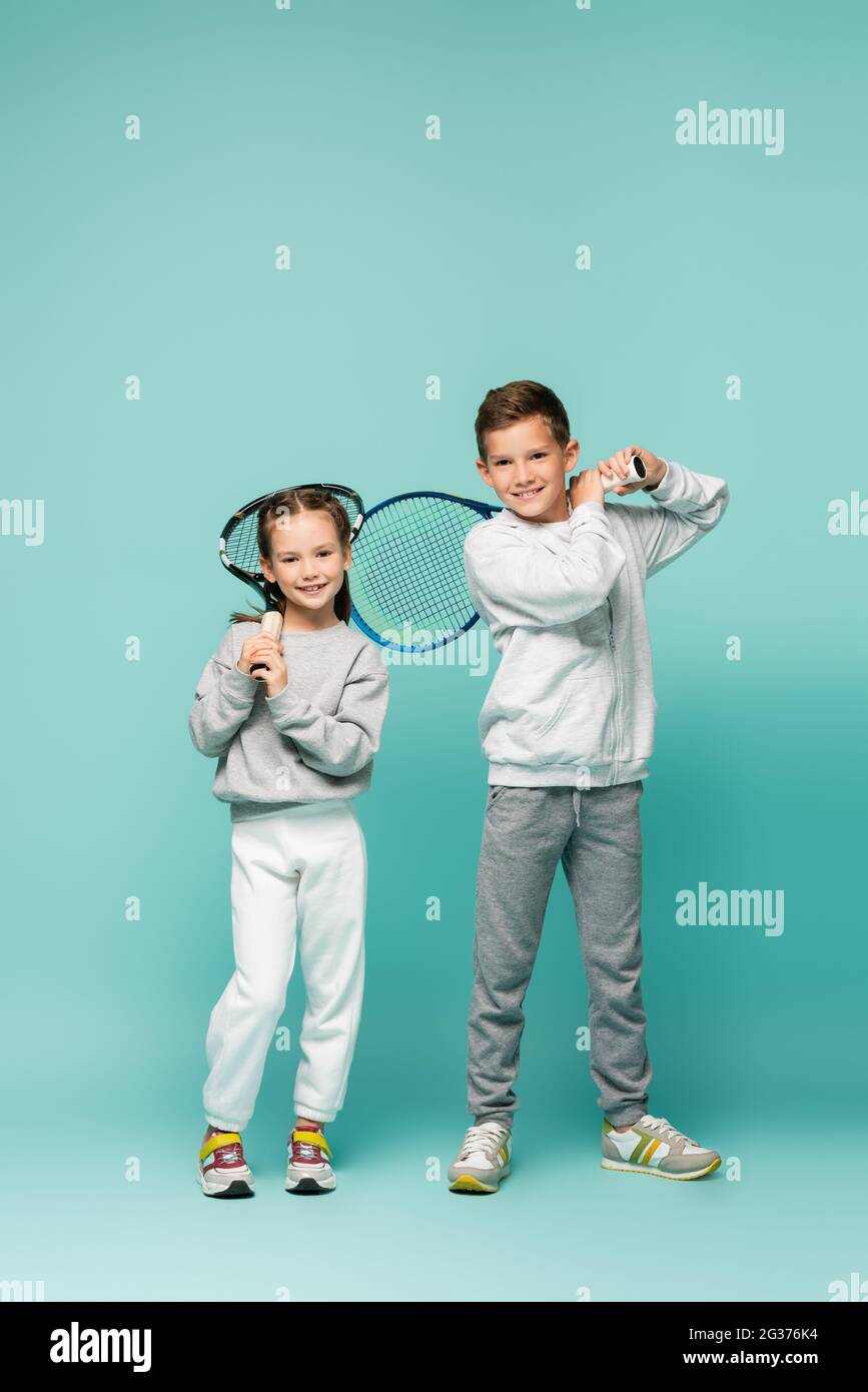 felici i bambini in abbigliamento sportivo in piedi con racchette da tennis su blu Foto Stock