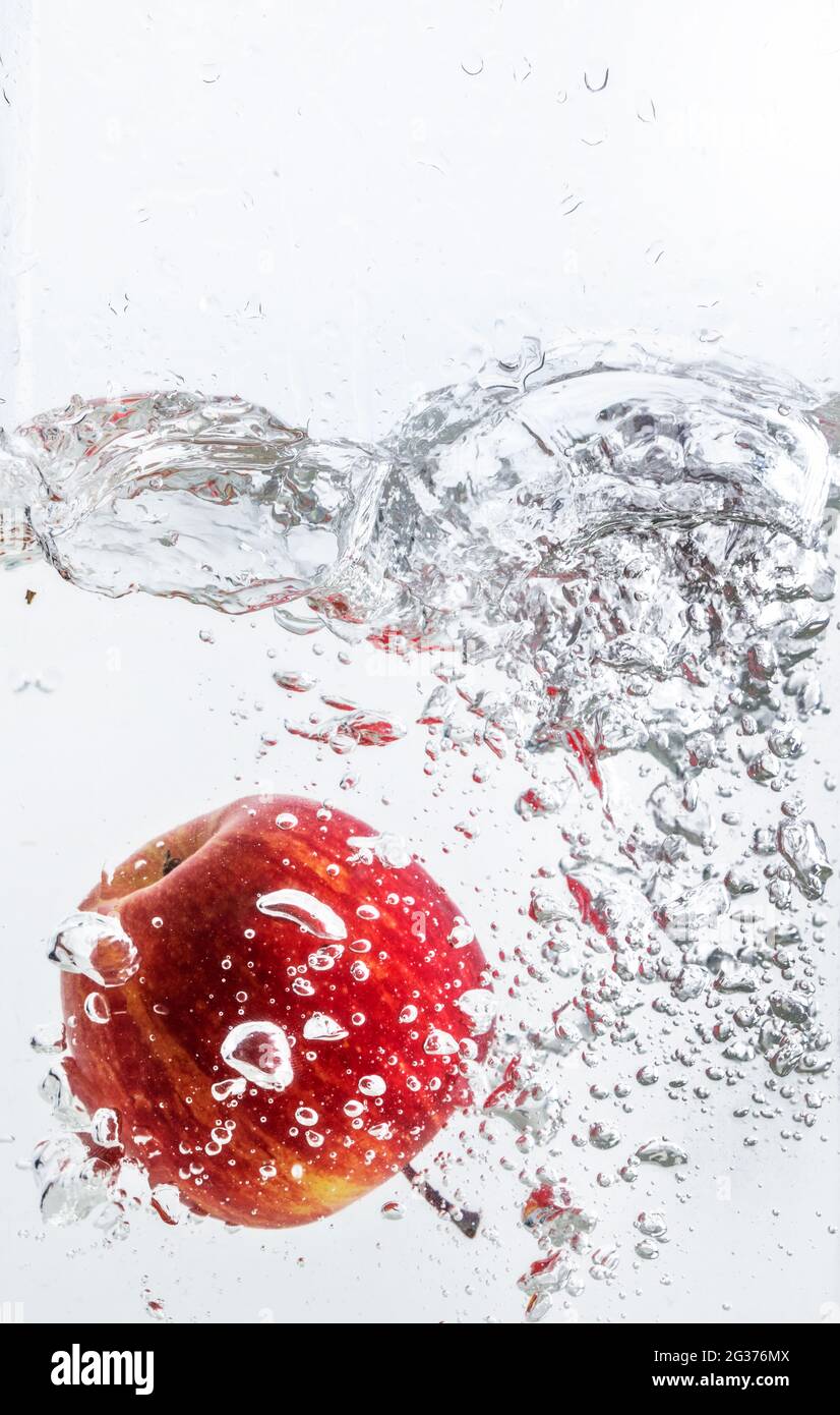 Spruzzi d'acqua con mela rossa e sfondo bianco. Foto Stock