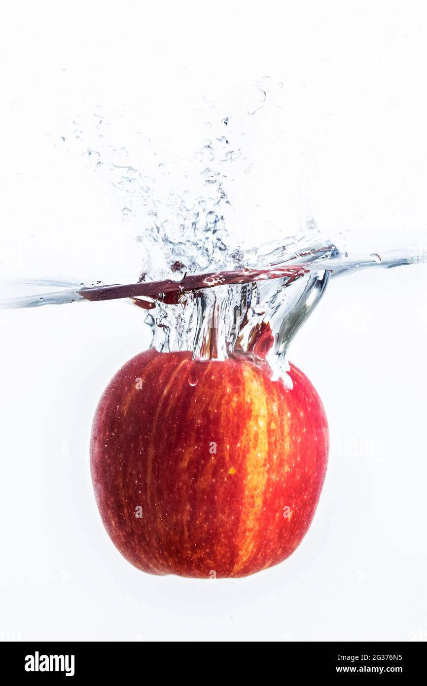 Spruzzi d'acqua con mela rossa e sfondo bianco. Foto Stock