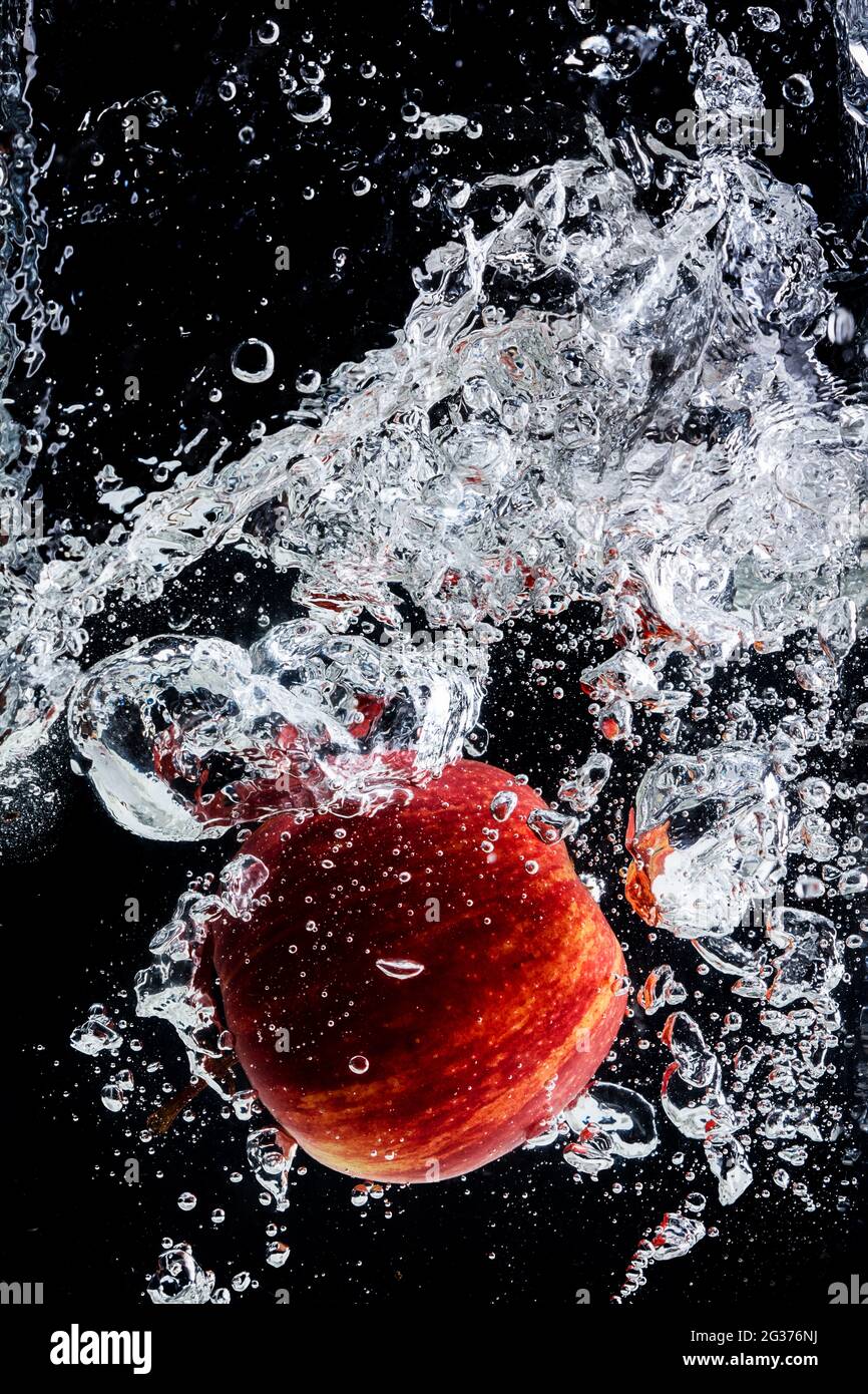 Spruzzi d'acqua con mela rossa e sfondo nero. Foto Stock
