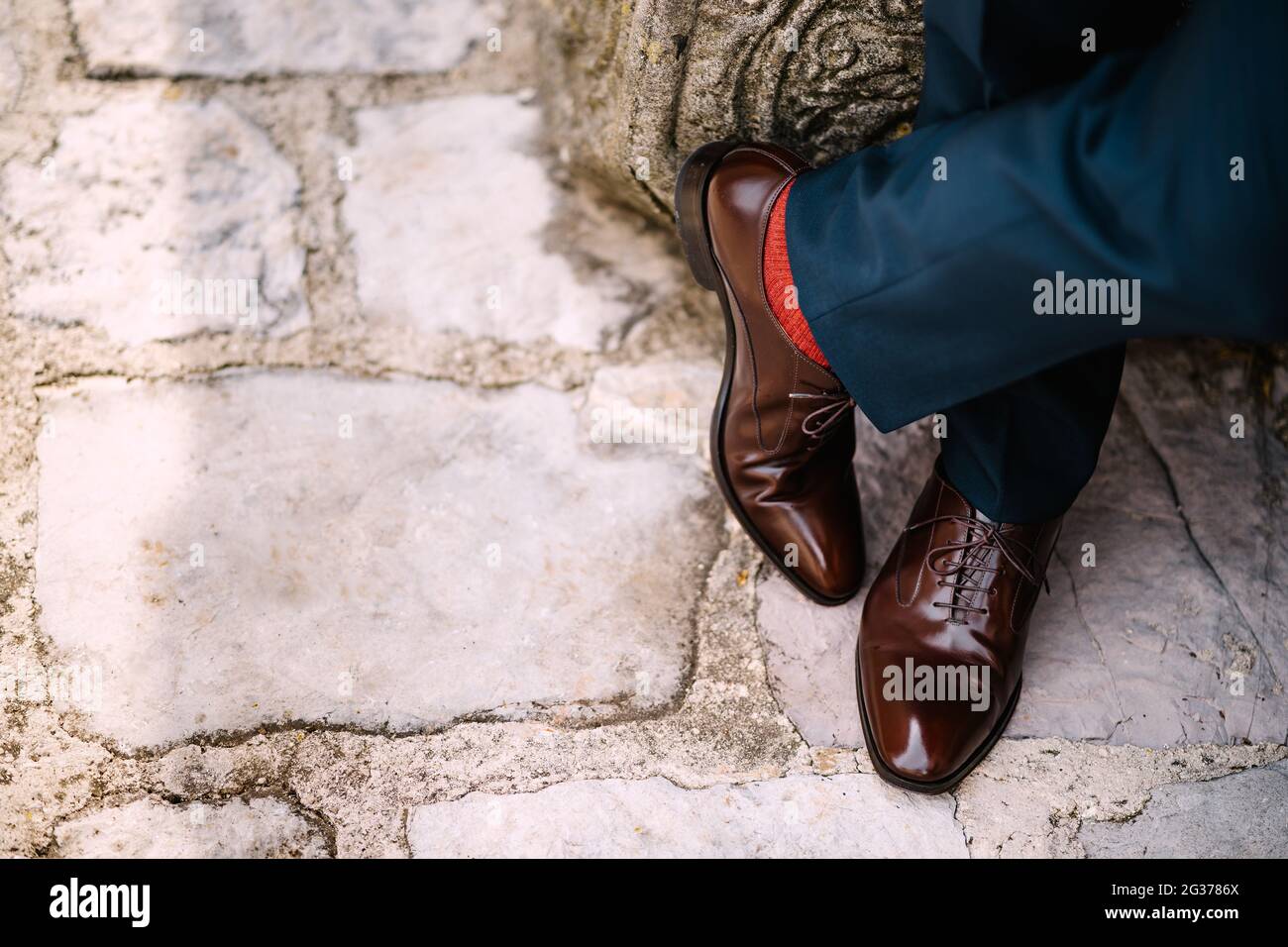 Gambe incrociate di un uomo in pantaloni blu, calze rosse e scarpe marroni  in piedi sulla strada di pietra, vista dall'alto Foto stock - Alamy
