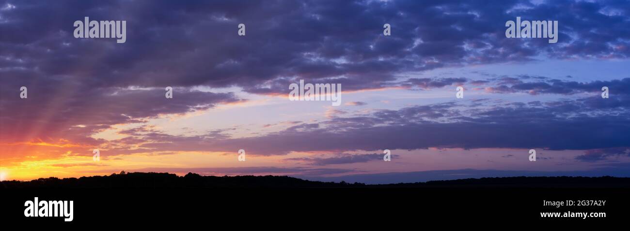 Panorama di un bellissimo tramonto con nuvole viola e raggi solari all'orizzonte Foto Stock
