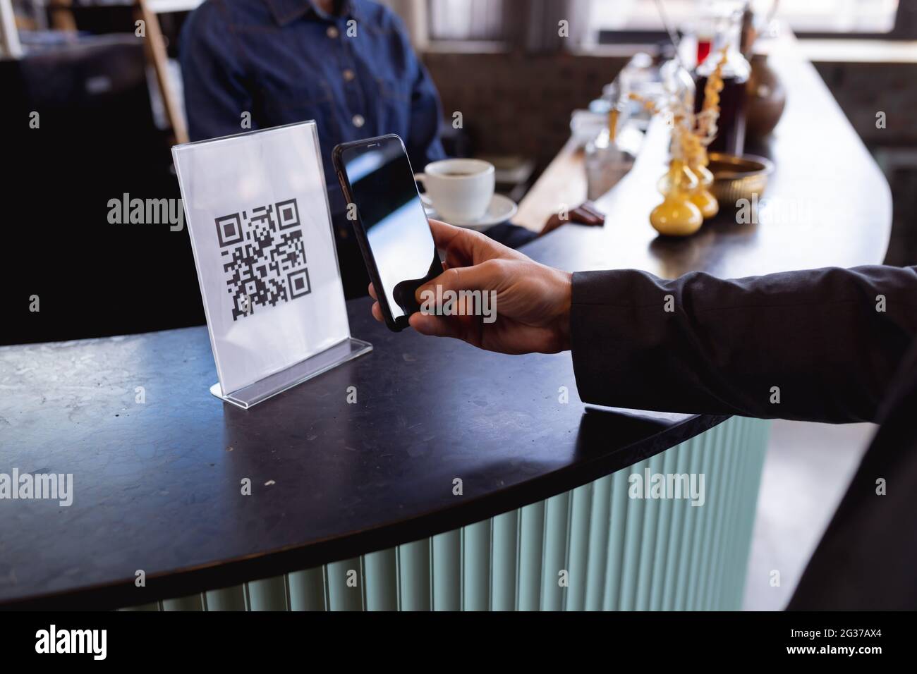 Sezione centrale dell'uomo che effettua un pagamento tramite la scansione del codice qr dallo smartphone in un bar Foto Stock