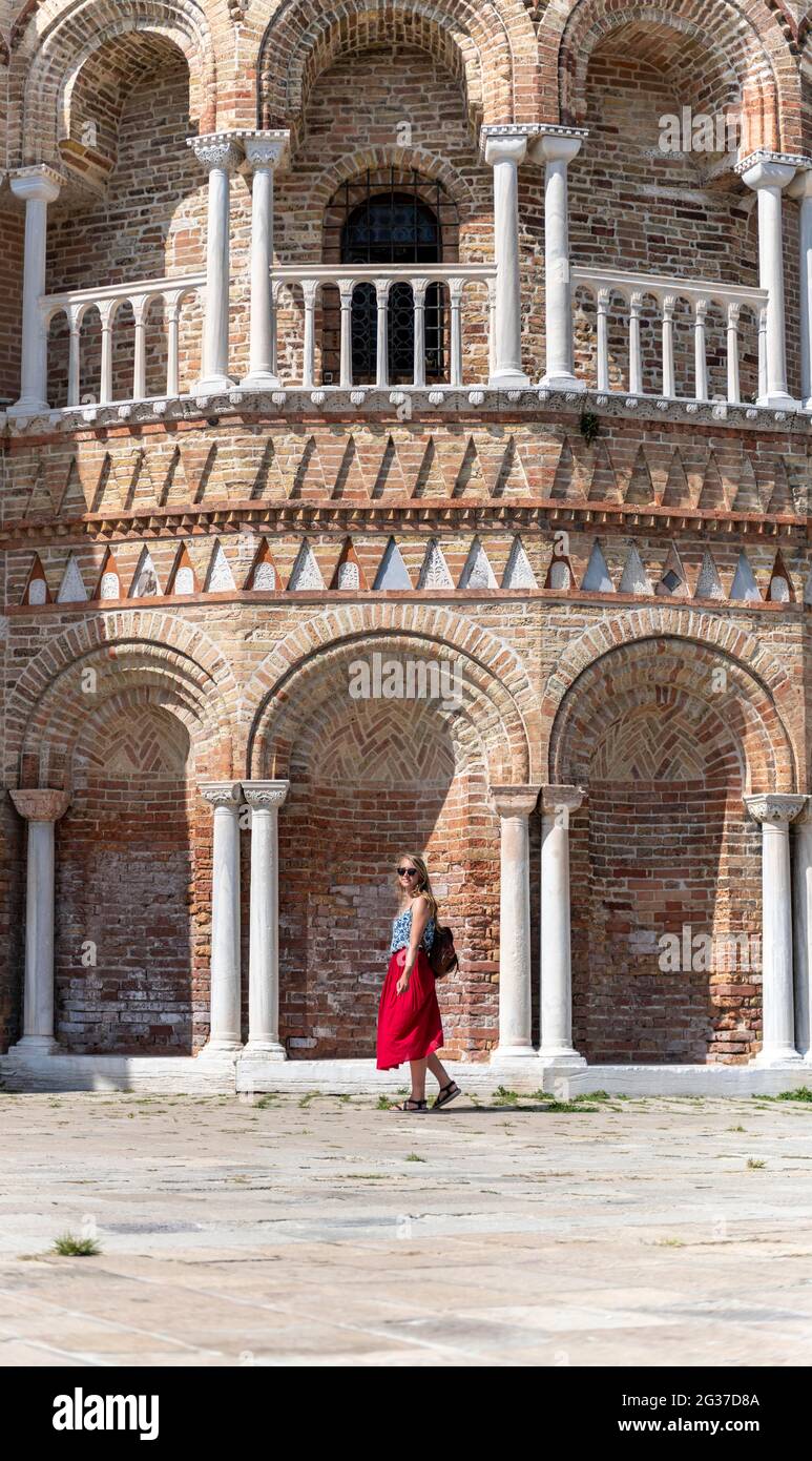 Giovane donna in abito rosso di fronte alla Basilica dei Santi Maria e Donato, Murano, Isola di Murano, Venezia, Veneto, Italia Foto Stock