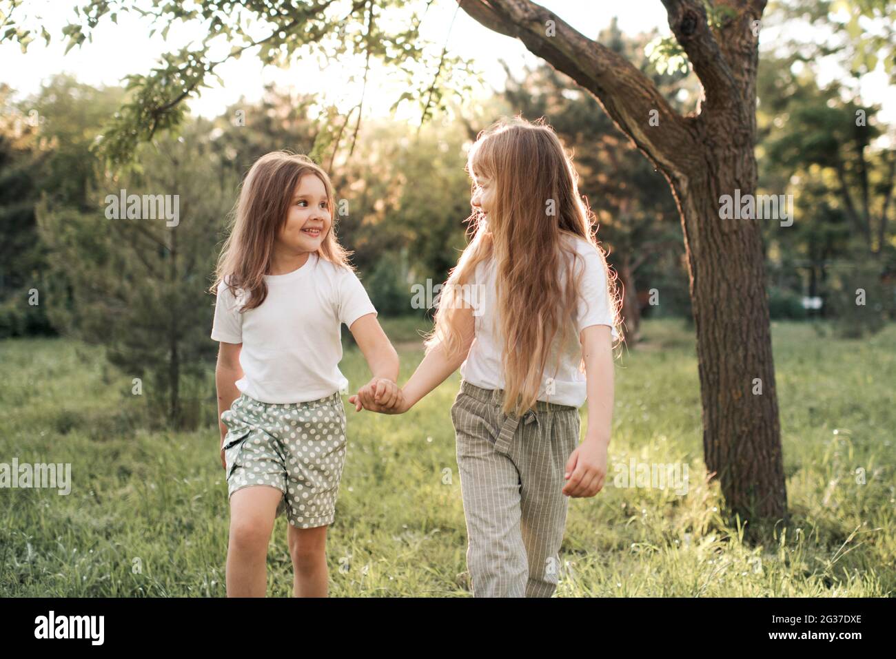 Felice sorridente bambine 5-6 anni tenendo le mani camminare nel parco su sfondo natura insieme. Guardarsi l'un l'altro. Amicizia. La togetherness. Presc Foto Stock