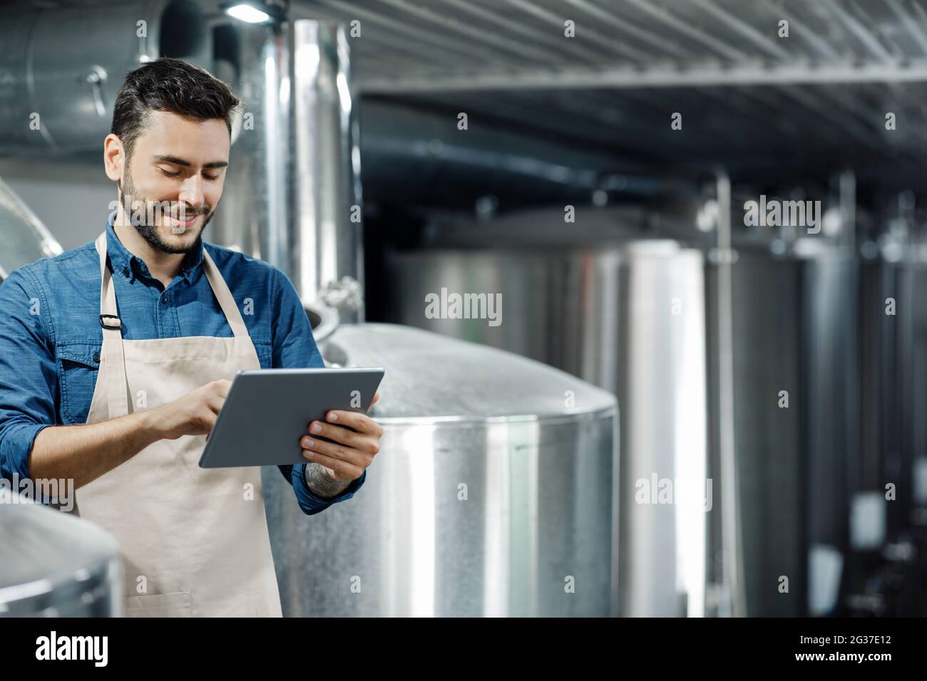 Il giovane lavora alla fabbrica di birra. Birrificio, attrezzature industriali e moderno dispositivo digitale intelligente presso la fabbrica di birra Foto Stock