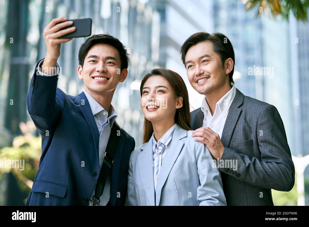 squadra di tre uomini d'affari asiatici che prendono un selfie in centro quartiere finanziario della città moderna Foto Stock