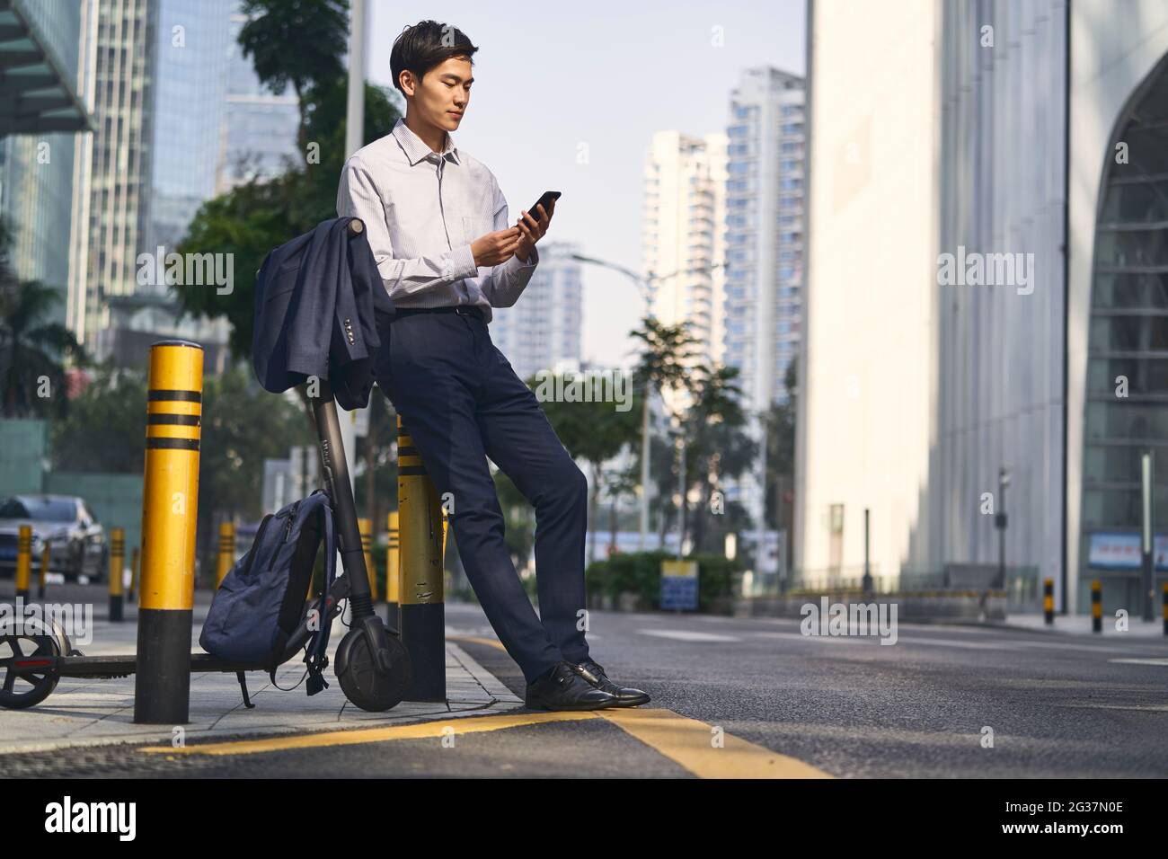 giovane uomo d'affari asiatico in piedi accanto al suo scooter elettrico strada nel downtow della città moderna Foto Stock