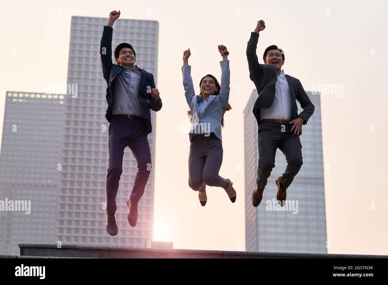 team di tre dirigenti aziendali asiatici che saltano celebrando il successo e il successo con il background della città Foto Stock