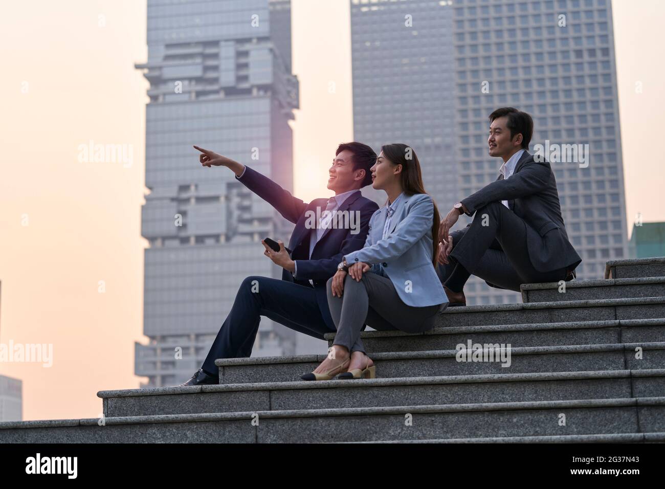 team di tre dirigenti aziendali asiatici seduti su gradini parlare chattando rilassante Foto Stock